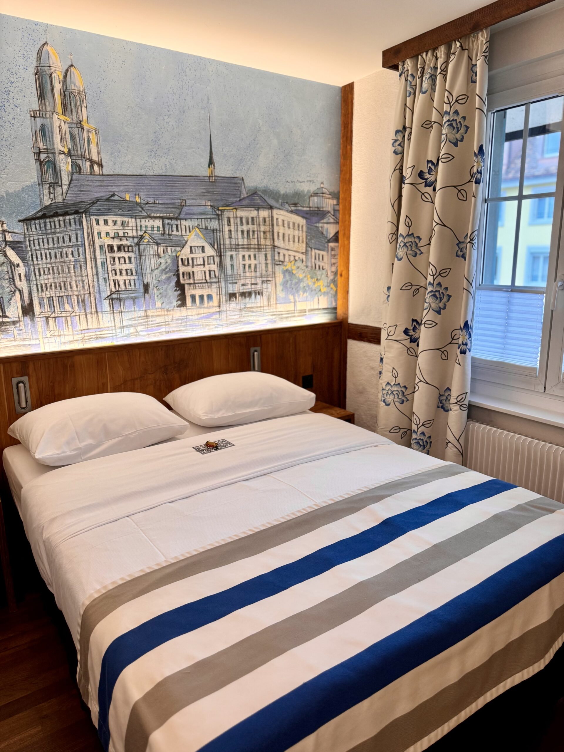 Bed in hotel room with mural of Zurich